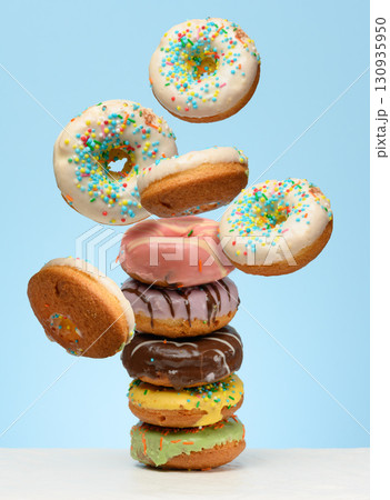 A stack glazed donuts on a table. White donuts with sprinkles flying around them A stack glazed donuts on a table. White donuts with sprinkles flying around them 130935950