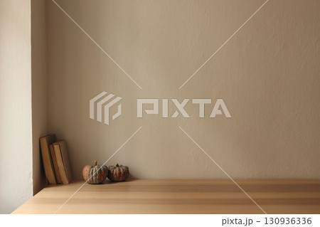 Autumn interior still life. Scandinavian living room, home office. Pumpkins, old books on table, desk. Fall, Halloween or Thanksgiving holiday home decor. Empty beige wall mockup background. 130936336
