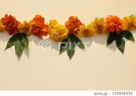 Traditional Indian marigold floral garland toran. Yellow orange zendu flowers, green leaves. Beige background. Festive culture symbol. Diwali, weddings, Dia de los Muertos Halloween celebrations decor Traditional Indian marigold floral garland toran. Yellow orange zendu flowers, green leaves. Beige background. Festive culture symbol. Diwali, weddings, Dia de los Muertos Halloween celebrations decor 130936339