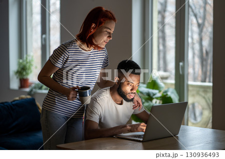 Loving woman wife standing behind husband working on laptop, supporting him in online business 130936493
