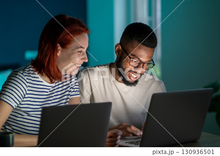 Happy diverse couple have small online business at home work on laptops in evening Happy diverse couple have small online business at home work on laptops in evening 130936501