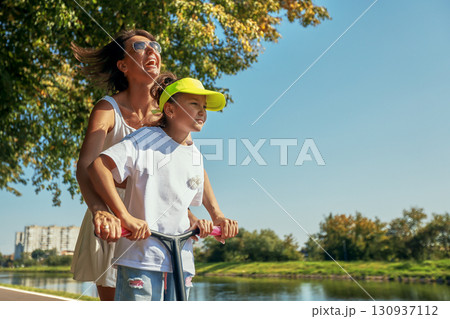 Mother and daughter enjoying a scooter ride along a summer riverside path Mother and daughter enjoying a scooter ride along a summer riverside path 130937112