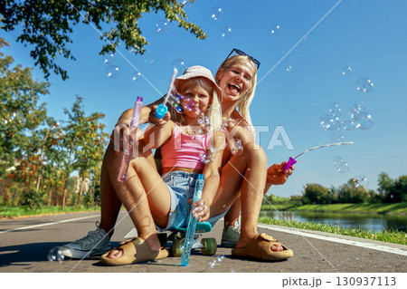 Mother and daughter bonding outdoors, blowing bubbles on a sunny day Mother and daughter bonding outdoors, blowing bubbles on a sunny day 130937113