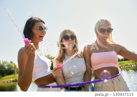 Three friends enjoying a sunny day outdoors with bubbles and smiles 130937115