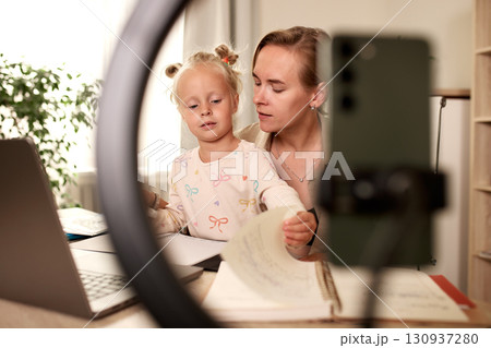 Mother assisting young daughter with remote learning at home workplace setup 130937280