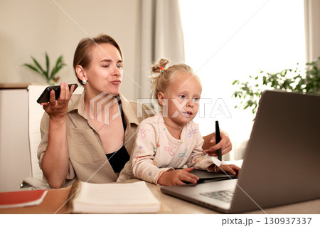 Mother multitasking with work while caring for her daughter at home Mother multitasking with work while caring for her daughter at home 130937337