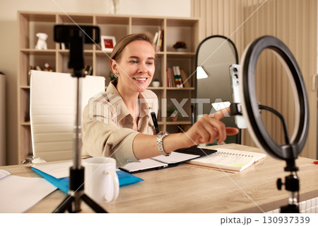 Woman recording a video in home office with ring light and smartphone Woman recording a video in home office with ring light and smartphone 130937339