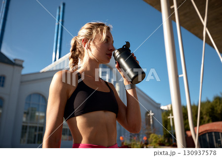 Focused athlete drinking from a shaker bottle outdoors on a sunny day 130937578