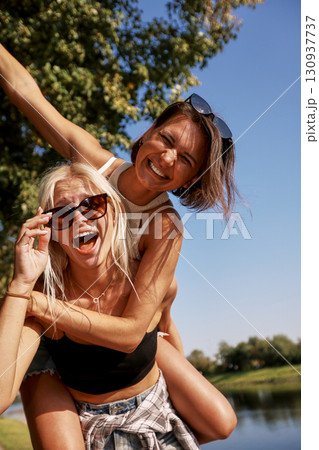 Two joyful women enjoying a sunny outdoor moment by the water Two joyful women enjoying a sunny outdoor moment by the water 130937737