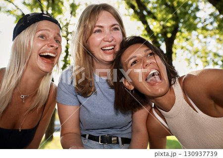 Three young women laughing outdoors in a cheerful summer setting 130937739