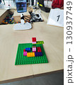 Small LEGO structure on a green baseplate displayed on a wooden table. The structure consists of various colored bricks, including red, pink, blue, yellow, and purple. Plastic cubes  130937749
