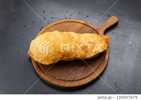 Traditional deep fried cheburek with golden crust served on wooden board, top view Traditional deep fried cheburek with golden crust served on wooden board, top view 130937879