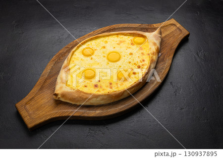 Traditional Georgian Adjarian khachapuri with eggs and cheese on a wooden board Traditional Georgian Adjarian khachapuri with eggs and cheese on a wooden board 130937895