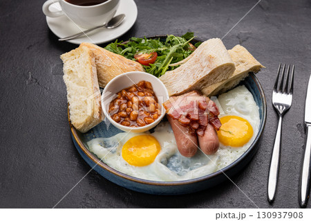 Traditional English breakfast with eggs, bacon, beans, toast, and tea on a dark background 130937908