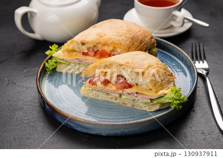 Ciabatta sandwich with cheese, ham and lettuce served with tea on a rustic black background 130937911