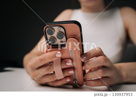 Woman holding new mobile phone featuring stylish case with convenient hand strap, ensuring secure grip while showcasing fashionable and modern look. Concept of modern technology 130937953