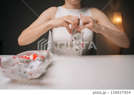 Woman unpacking new white triple electrical outlet extender sitting at white table, with lamp softly illuminating background in cozy dark indoor setting, close-up. Concept of modern technology. 130937954