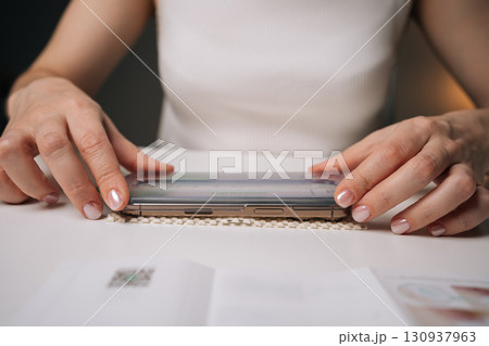 Woman applying screen protector to modern smartphone, ensuring precise alignment for optimal protection against scratches and potential damage to device display. Concept of mobile phone maintenance. 130937963