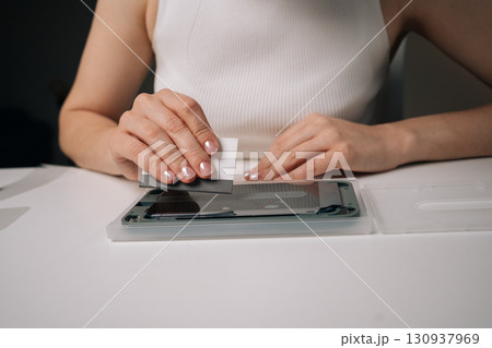 Technician young woman using specialized machine and squeegee to meticulously apply screen protector to smartphone, ensuring perfect fit and bubble-free finish. Concept of mobile phone service. 130937969