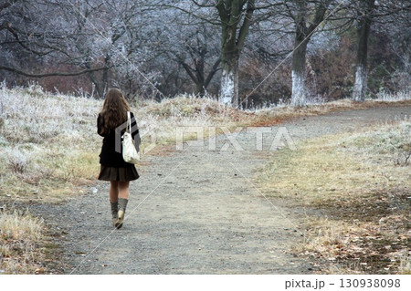 Young woman walks on a path through frosty trees 130938098
