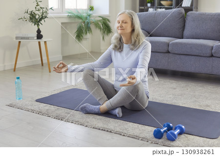Home yoga and meditation of happy senior woman, old person training on mat in lotus position 130938261