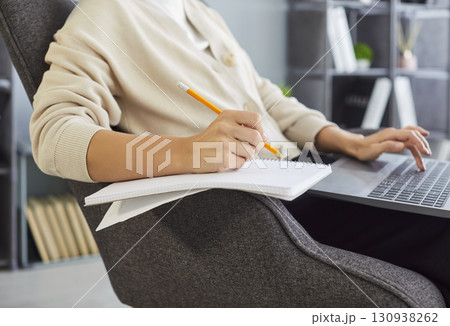 Sitting working in comfortable grey chair, focused work, writing in notebook typing on laptop Sitting working in comfortable grey chair, focused work, writing in notebook typing on laptop 130938262
