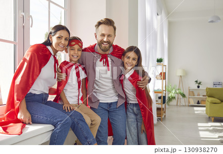 Happy family in superhero costumes sitting on the windowsill at home and looking at camera. Happy family in superhero costumes sitting on the windowsill at home and looking at camera. 130938270