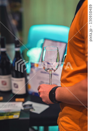 Person in an orange shirt holds an empty wine glass during a wine tasting event. Concept of wine, tasting, lifestyle centered around social gatherings and wine culture 130938489