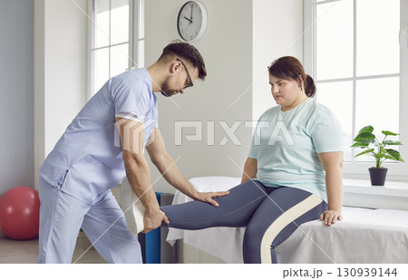 Young professional physiotherapist prepare fat woman patient for gym exercises. Young professional physiotherapist prepare fat woman patient for gym exercises. 130939144