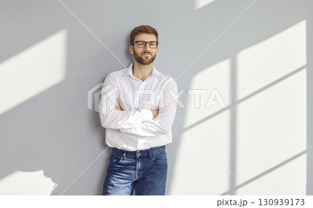 Confident bearded man in eyeglasses posing with crossed arms at gray wall Confident bearded man in eyeglasses posing with crossed arms at gray wall 130939173