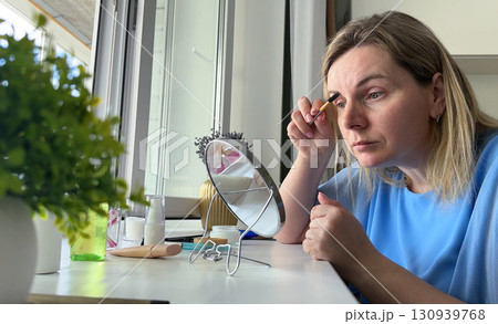 The girl carefully blends eyeshadow, her reflection showing concentration and excitement for her upcoming event. 130939768