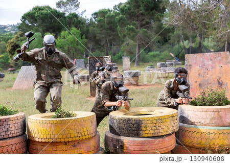 Expressive paintball team running with a marker guns at open playing field 130940608