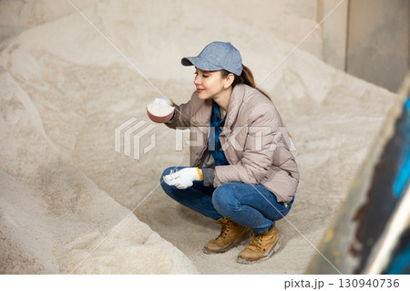 Woman using scoop to collect corn flour in an animal feed warehouse 130940736