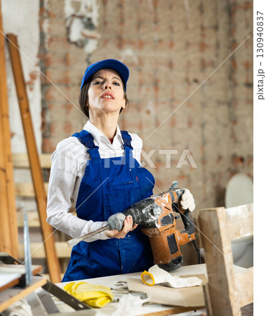 Workwoman standing at construction site with pneumatic chisel hammer 130940837