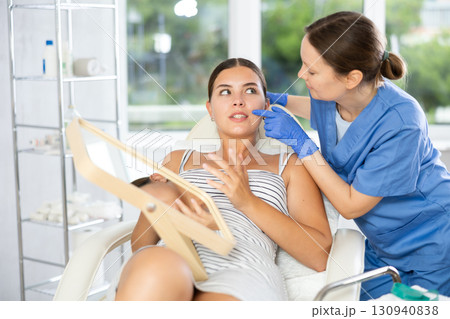 Adult female cosmetologist examining face of female patient Adult female cosmetologist examining face of female patient 130940838