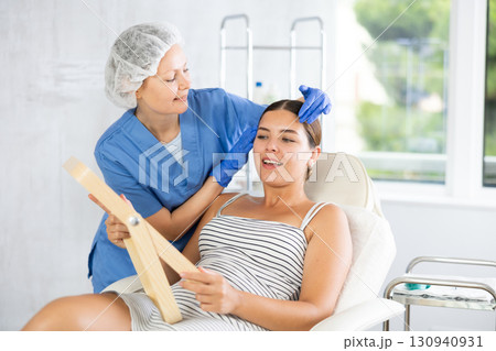 Adult female cosmetologist examining face of female patient 130940931