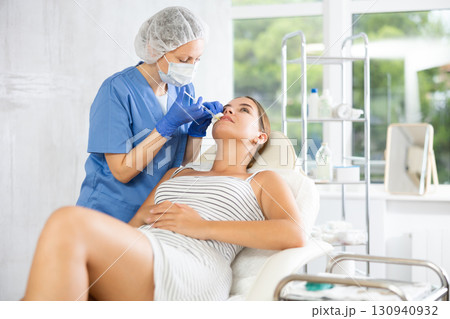 Adult woman cosmetologist makes injection in lips of patient Adult woman cosmetologist makes injection in lips of patient 130940932