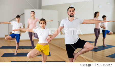 Teen girl with father standing in Eka Pada Pranamasana holding hands 130940967
