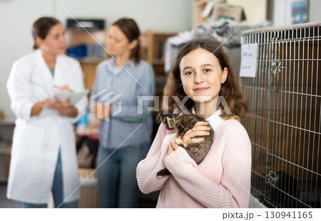 Preteen girl standing in animal shelter with kitten in hands 130941165