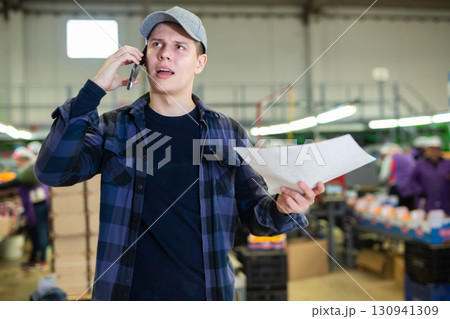 Positive cheerful men worker conducts business negotiations on the phone on fruit processing plant. 130941309