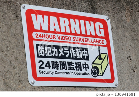 コンクリートの壁に貼られた、「防犯カメラ作動中」の警告標示板 130941681
