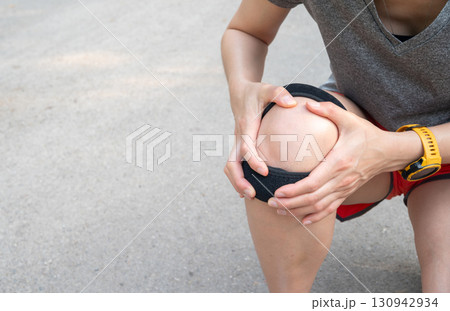 Runner woman holding her knee while she having suffering from knee pain and she wearing knee braces for supports to be worn when you have pain in your knee. Runner woman holding her knee while she having suffering from knee pain and she wearing knee braces for supports to be worn when you have pain in your knee. 130942934