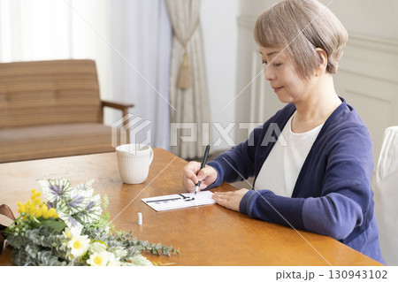 不祝儀袋に筆ペンで表書きをするシニア女性 130943102