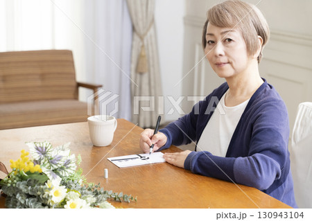 不祝儀袋に筆ペンで表書きをするシニア女性 130943104