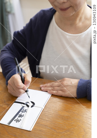 不祝儀袋に筆ペンで表書きをするシニア女性 不祝儀袋に筆ペンで表書きをするシニア女性 130943109