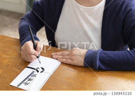 不祝儀袋に筆ペンで表書きをするシニア女性 130943110