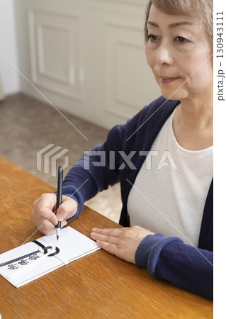 不祝儀袋に筆ペンで表書きをするシニア女性 130943111