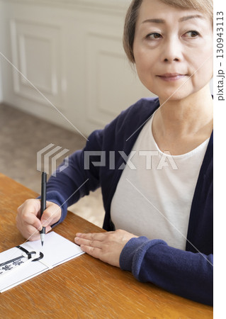 不祝儀袋に筆ペンで表書きをするシニア女性 130943113