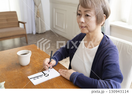 不祝儀袋に筆ペンで表書きをするシニア女性 130943114