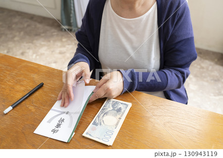 不祝儀袋に筆ペンで表書きをするシニア女性 130943119